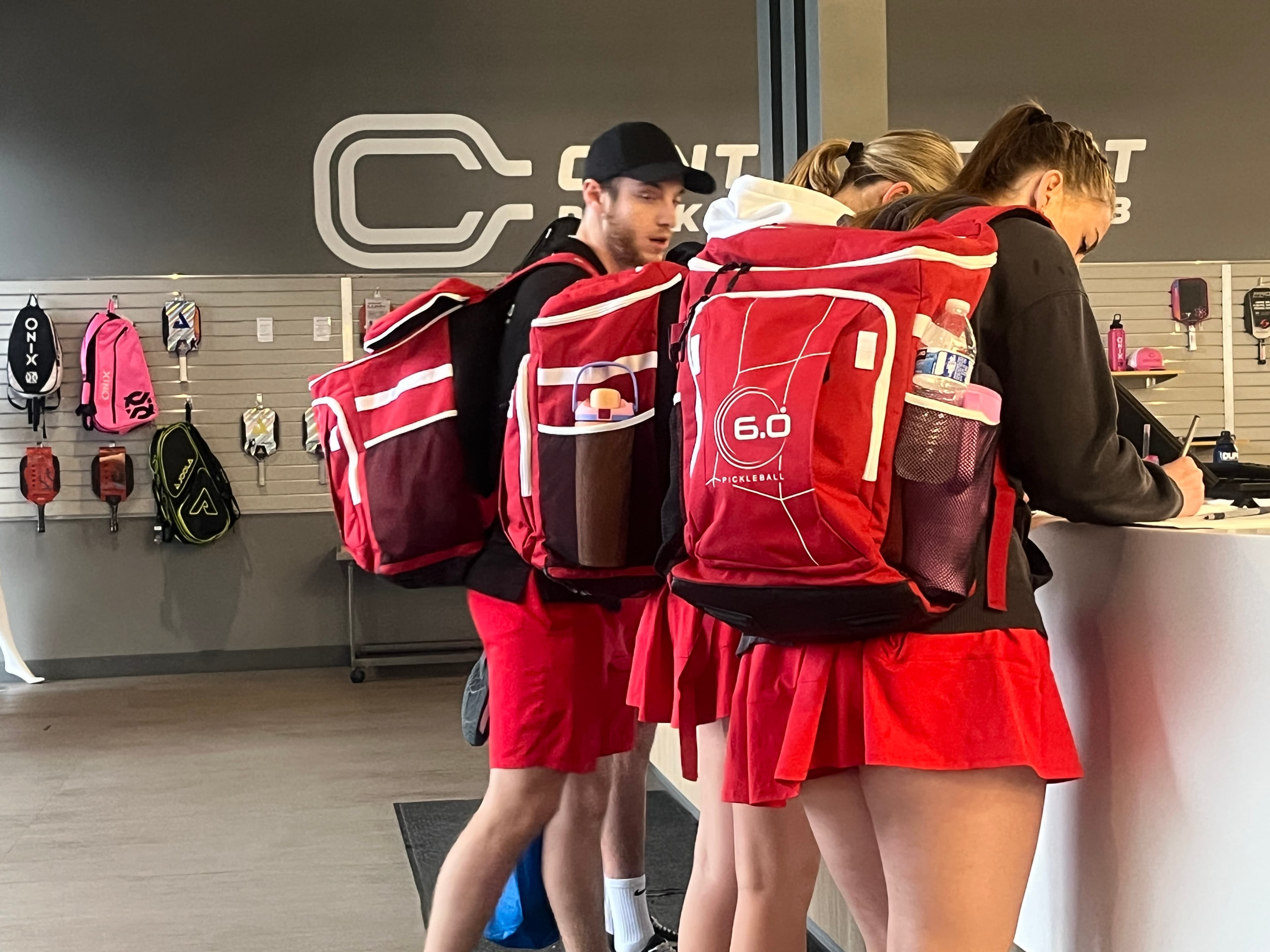 A college team in matching red kit checking in at a pickleball venue's front desk with their gear
